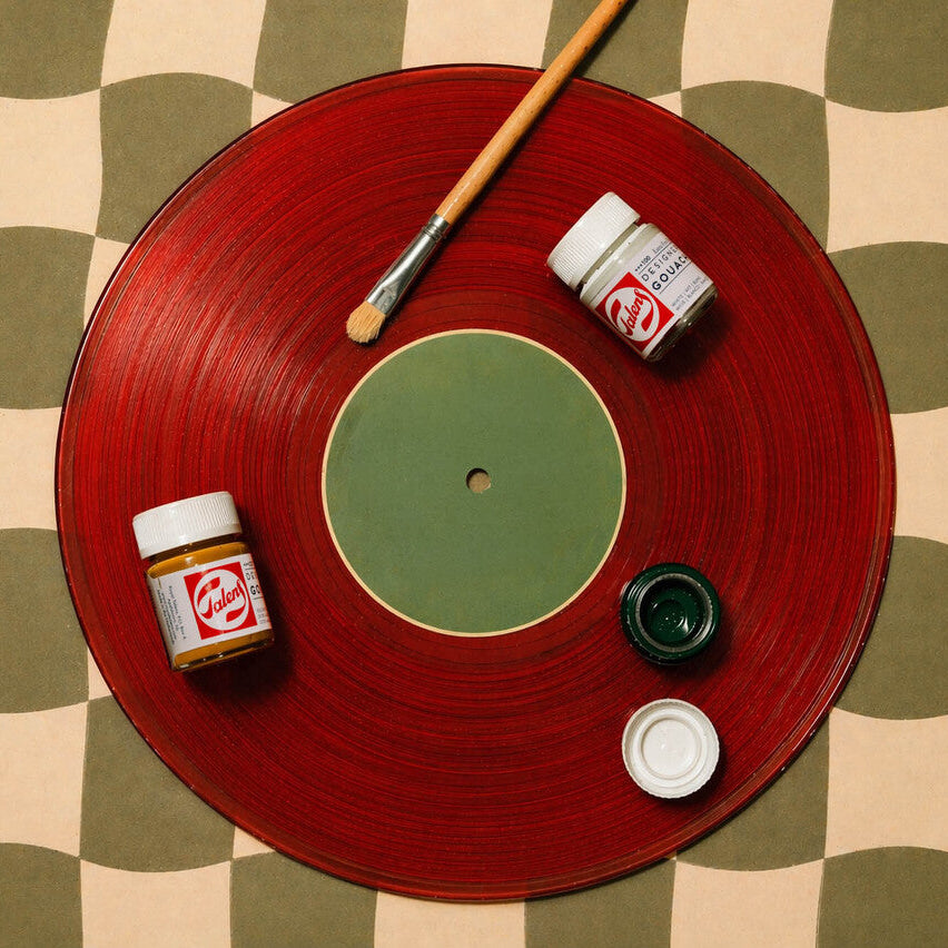Red vinyl record with paint can, brush, and small container on a checkered surface
